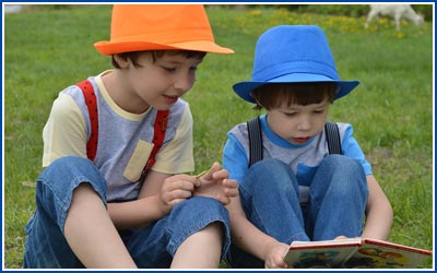 Two Boys reading a book while sitting on grass